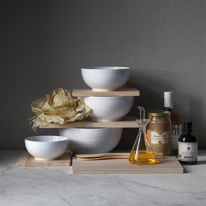 Royal Copenhagen Hvit Riflet Skål 18cm, stilfull samling av hvite skåler på treplater, ideelt for organisering av mat og ingredienser.