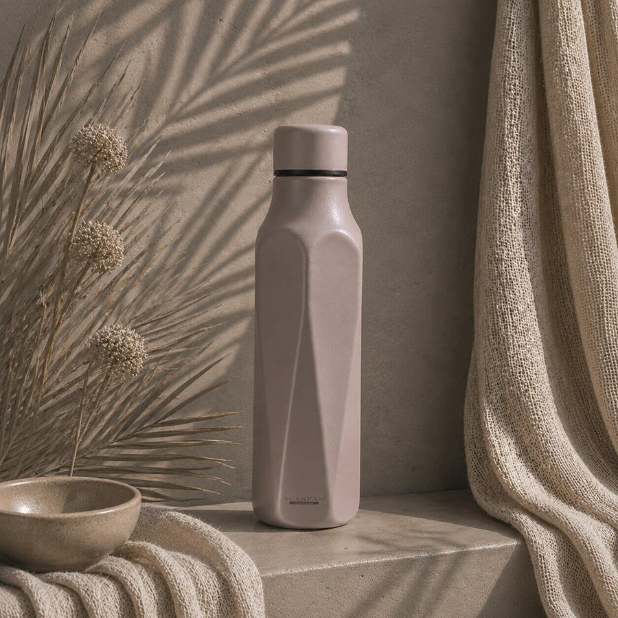 Stylish termoflaske i beige-grå Lava-toner plassert på en naturlig overflate, omringet av dekorative elementer, ideell for aktive hverdager.