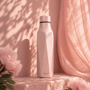 Scanpan Explore termoflaske 500 ml i rose, plassert mot en bakgrunn av myke stoffer og blomster, og fremhever dens stilige design.