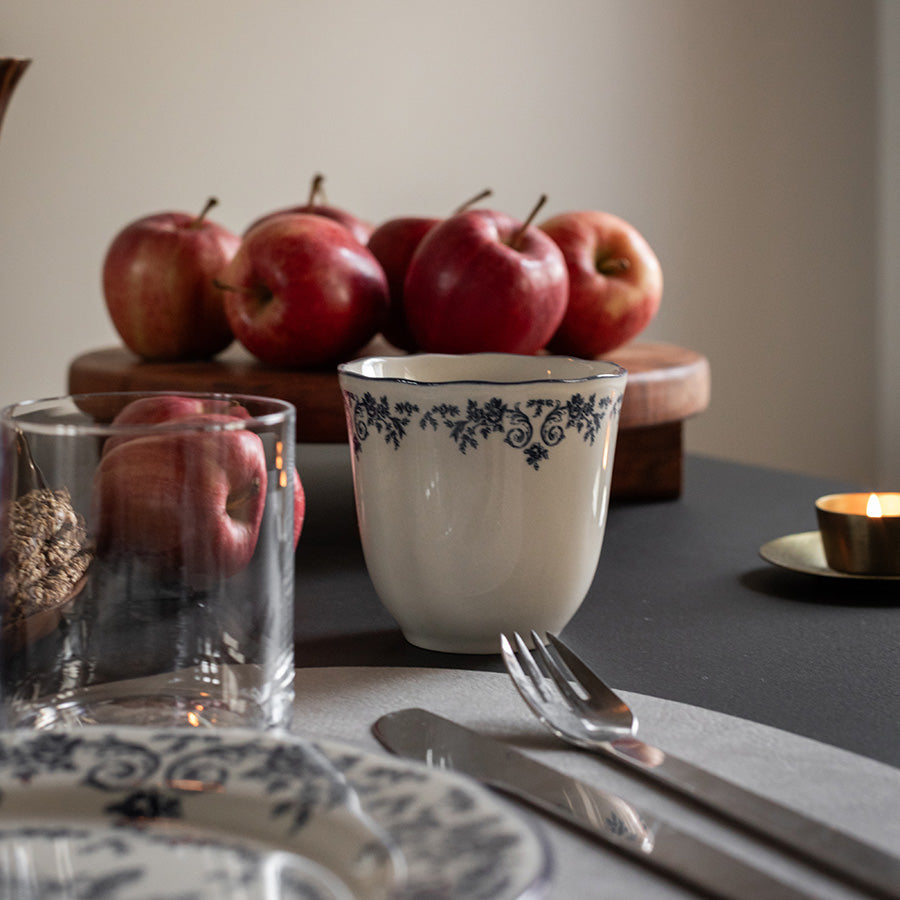 Blå blomsterprint kopp fra Seasons Fall Collection, stående på bordet sammen med epler og en glassbeholder, perfekt for daglig bruk.