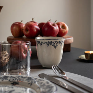 Blå blomsterprint kopp fra Seasons Fall Collection, stående på bordet sammen med epler og en glassbeholder, perfekt for daglig bruk.
