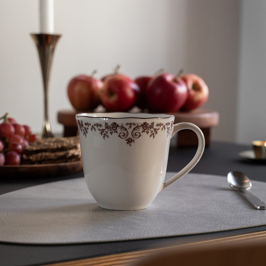 Seasons Fall Collection kopp med burgunderdekor, plassert på et stilfullt bord med epler i bakgrunnen. Ideell for varme drikker som kaffe eller te.