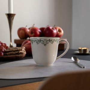 Seasons Fall Collection kopp med grønn blomsterdekor, plassert på et bord med røde epler og kjeks, ideell for kafferitualer.