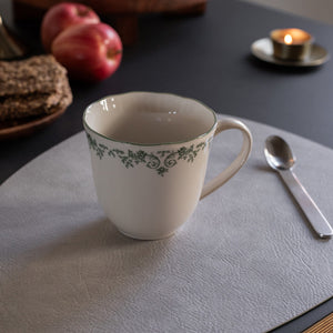 Nærbilde av Seasons Fall Collection kopp med grønn print, på et stilrent bord med epler og en skje, perfekt for melk eller te.