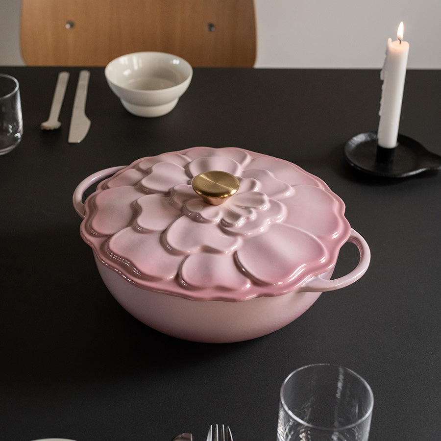 Elegant støpejernsgryte med blomsterdekor i rosa, plassert på bordet med tilbehør, perfekt for servering av deilig mat.