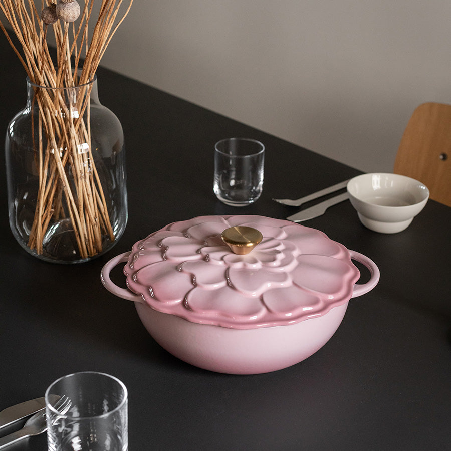 Støpejernsgryte med blomsterdekor, rosa emalje, dekorativt plassert på bordet med tallerkener og glass.
