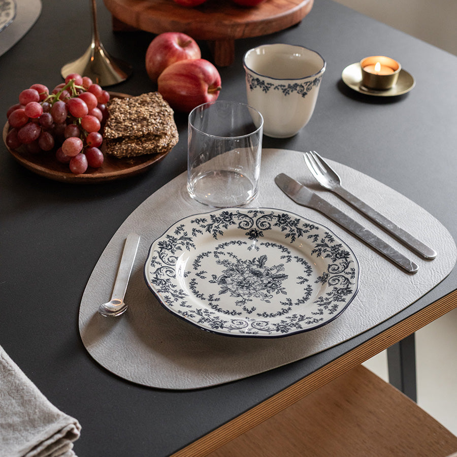 Tallerken fra Seasons med dekorative blomster, servert med frukt og kjeks på et moderne bord dekket med elegante bestikk og glass.