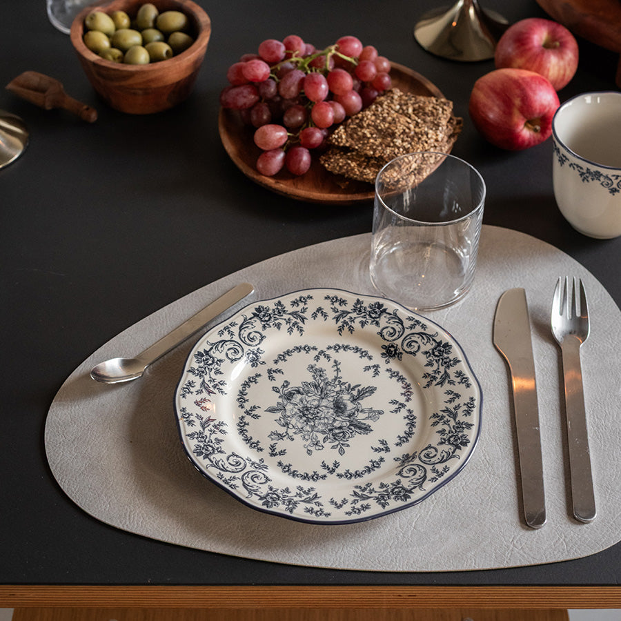 Tallerken fra Seasons med blå blomstermønster, servert med druer og kjeks på et elegant dekket bord.