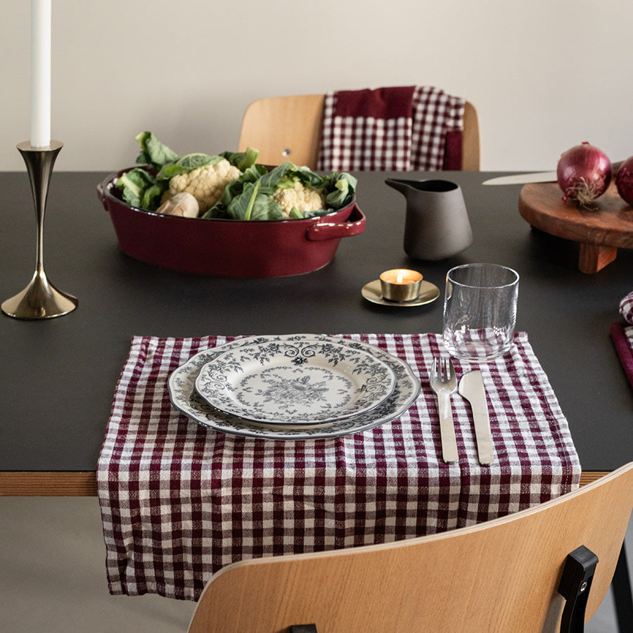 Seasons tallerken med blå blomsterdesign, plassert på et rutete kjøkkenhåndkle sammen med en stilfull kasserolle og tilbehør.