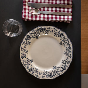Elegant tallerken med blå blomsterprint på hvit porselen, plassert på et dekket bord med riflet rød og hvit duk, bestikk og glass.