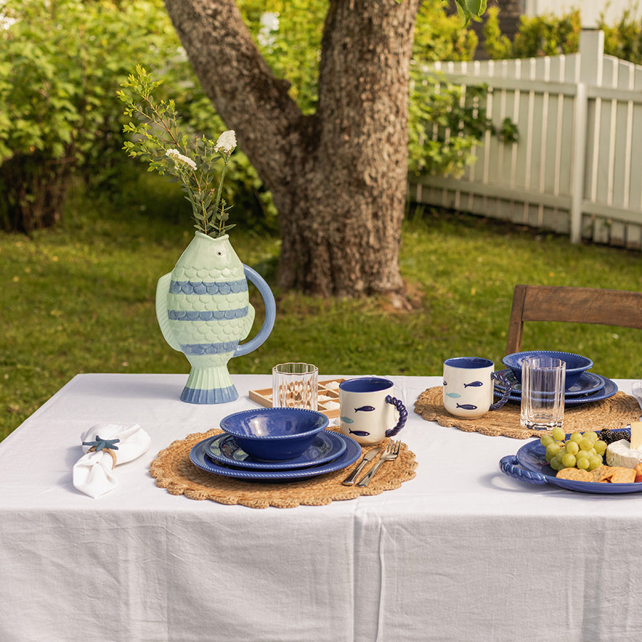 Vase Fisk Striper 31 cm fra Seasons, plassert på et bord i hagen, omgitt av tallerkener og glass, med grønne planter som gir en sommerlig atmosfære.