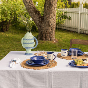 Vase Fisk Striper 31 cm fra Seasons, plassert på et bord i hagen, omgitt av tallerkener og glass, med grønne planter som gir en sommerlig atmosfære.