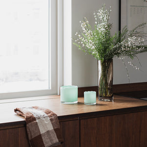 Flere lyslykter fra Seasons Spring Collection i lys grønn farge som står på en benk, sammen med en bukett av hvite blomster, skaper en varm og innbydende atmosfære.