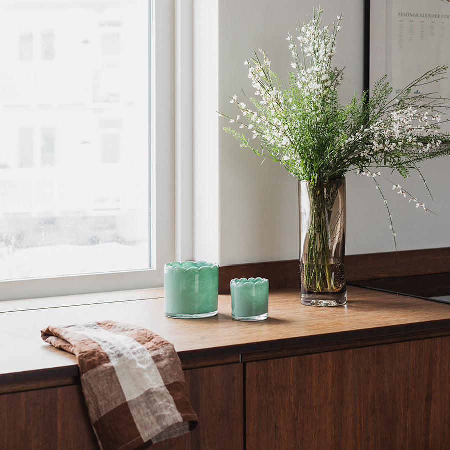 Seasons Lyslykt i mørk grønn, 11 cm høyde, plassert med vaser og blomster på et bord – skaper en lun atmosfære.