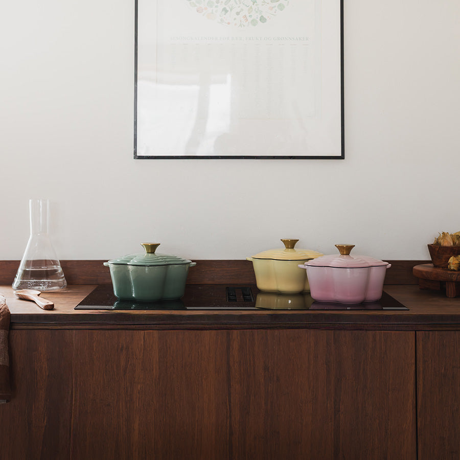 Seasons Støpejernsgryte Blomst 1,9L 30cm Rosa sammen med grønn og gul støpejernsgryte på en treoverflate.