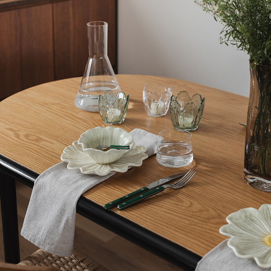 Detalj av Seasons lyslykter i klar glass, 8,5x8 cm, plassert ved siden av tallerkener og glass for en estetisk borddekorasjon.