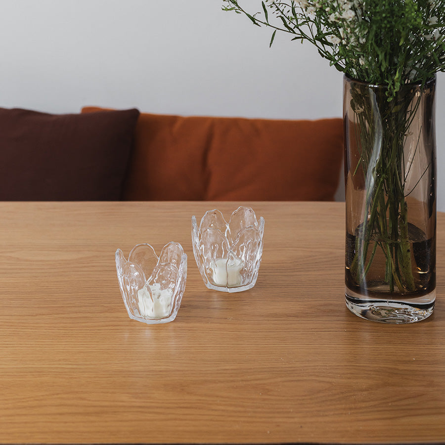 To Seasons lyslykter i klar glass, 8,5x8 cm, plassert på et trebord med en vase, skaper en hyggelig atmosfære.