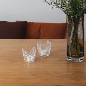 To Seasons lyslykter i klar glass, 8,5x8 cm, plassert på et trebord med en vase, skaper en hyggelig atmosfære.