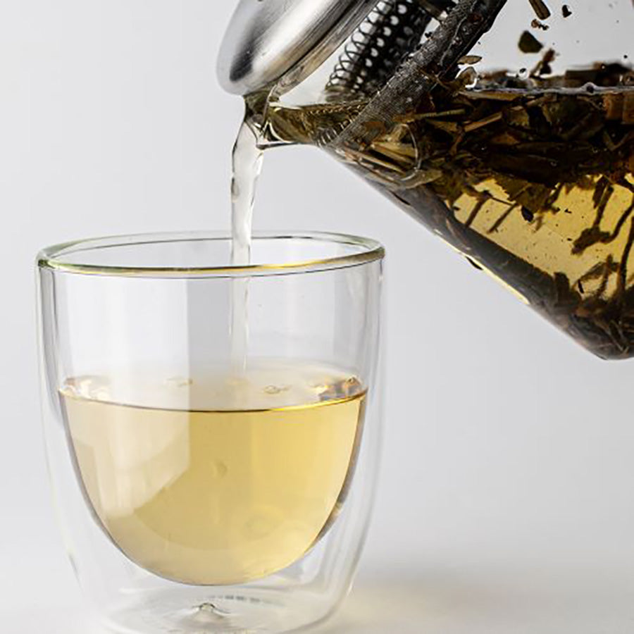 Hellende Teministeriet glass tekanne som heller te i en kopp, viser prosessen med brygging av løs te.