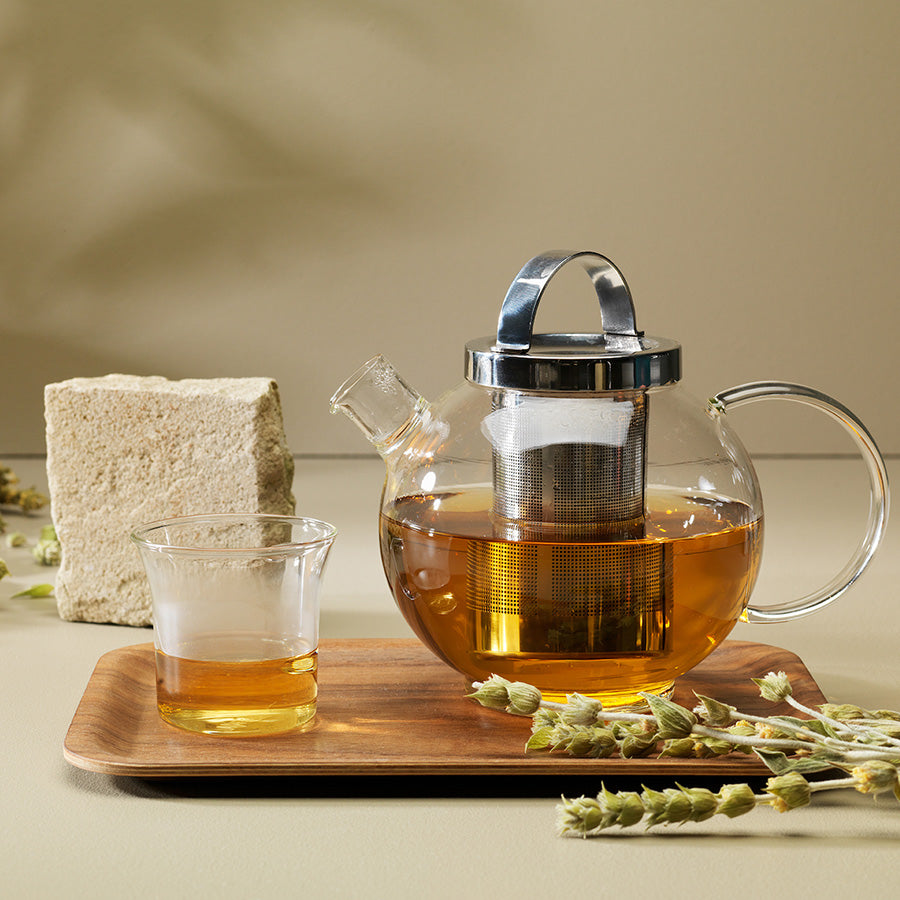 Elegant glass tekanne med en delikat sil, ved siden av en bedårende glasskrus og en naturlig dekorasjon, perfekt for å nyte deilig te.