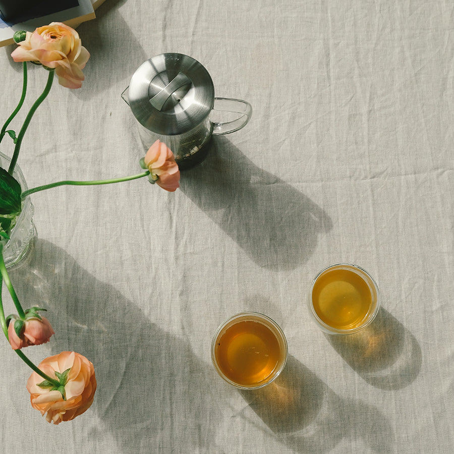 To glass med gylden te på et koselig, naturlig duket bord, med fine blomster som gir en innbydende atmosfære for tepause.