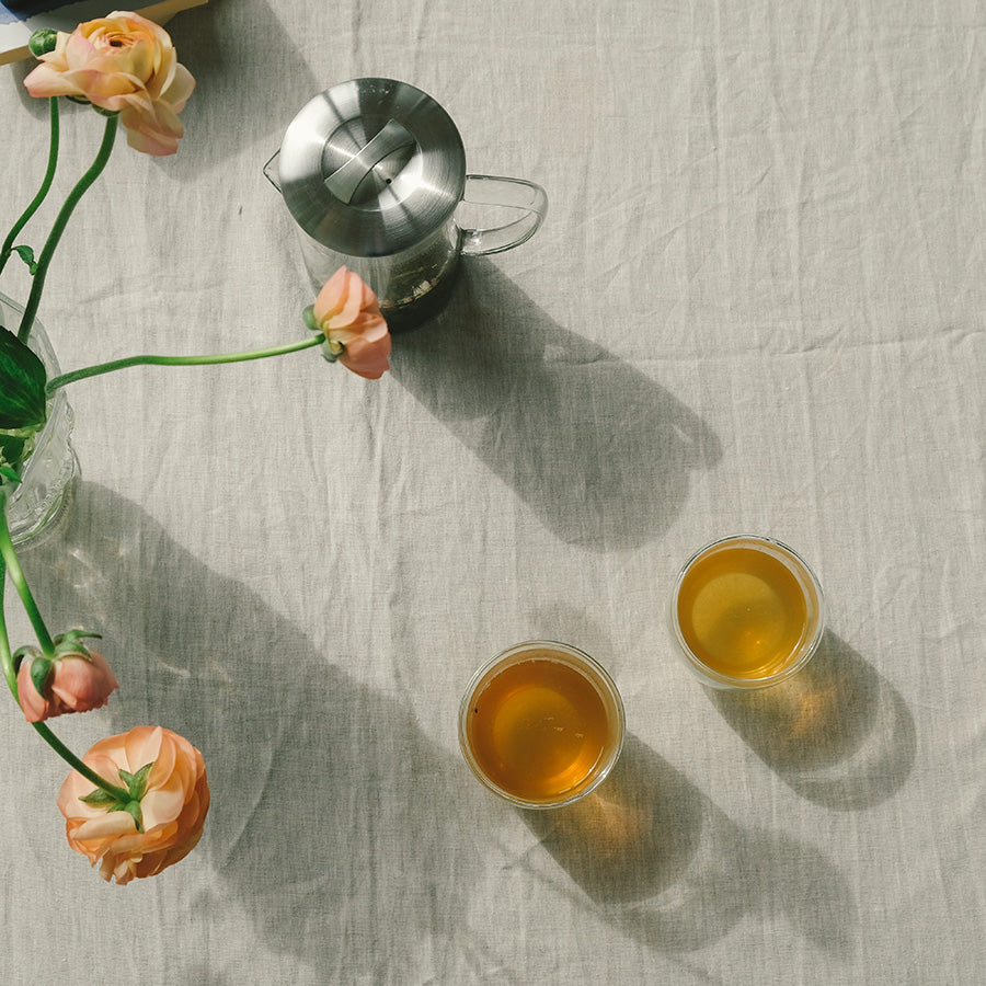 To glass med Teministeriet Moomin Rooibos Red Berries Te på et bord, med blomster og en tekanne i bakgrunnen.