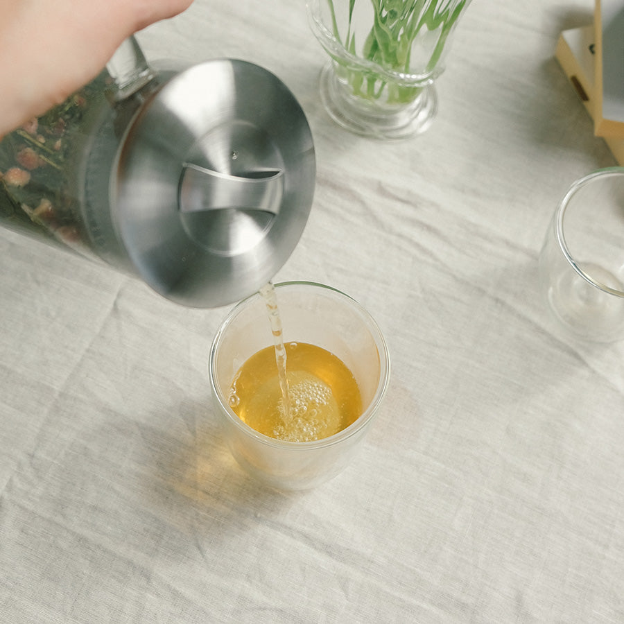 Heller Te fra en tekanne opp i et glass, viser den gyldne fargen og smaken av Teministeriet Moomin Mama Quince Sort Te.