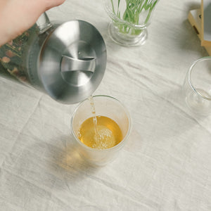 Heller Te fra en tekanne opp i et glass, viser den gyldne fargen og smaken av Teministeriet Moomin Mama Quince Sort Te.