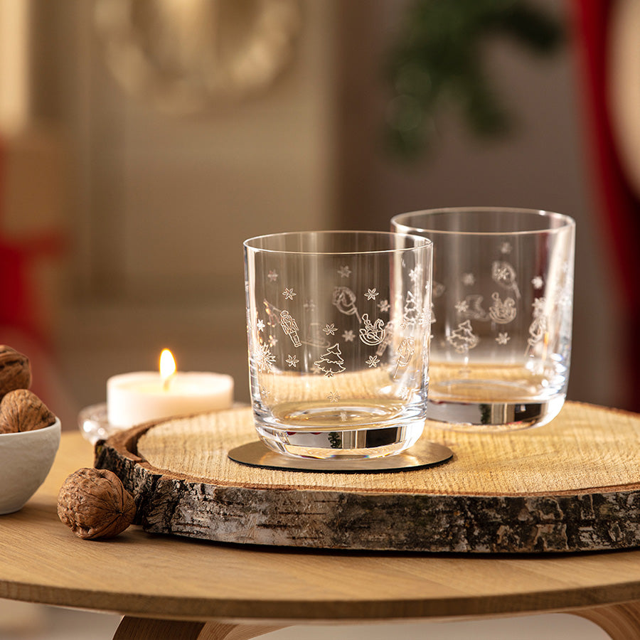 To Toy's Delight vannglass med julemotiv på trebord ved levende lys