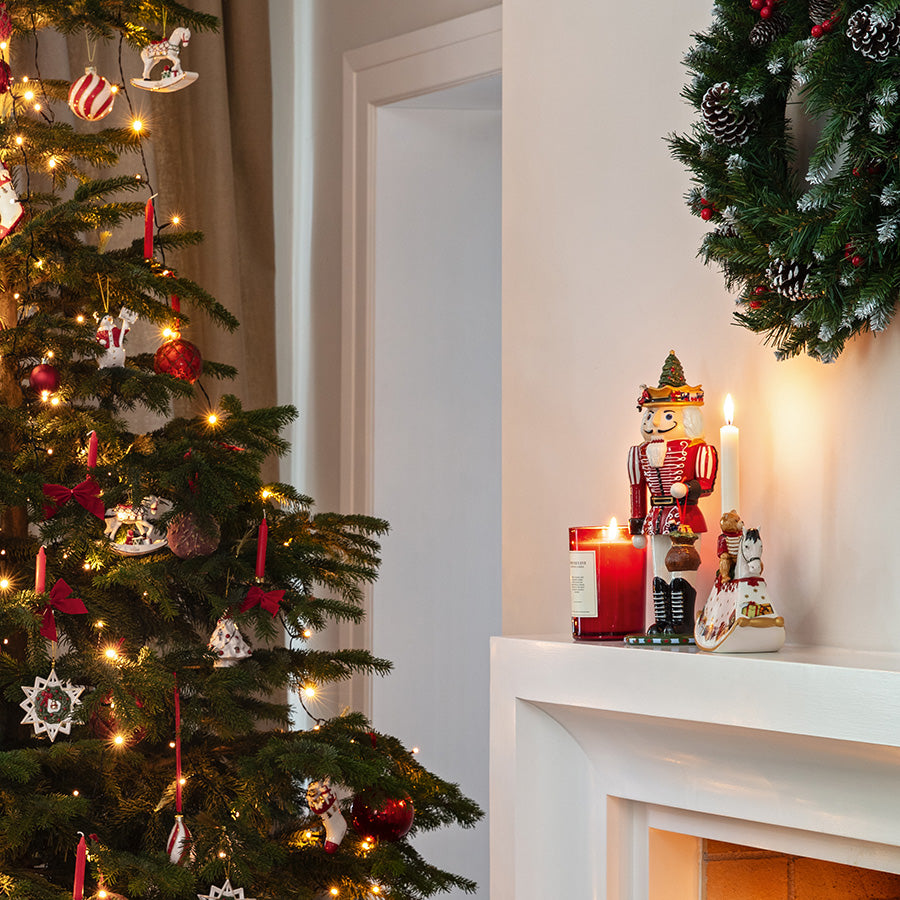 Rød Villeroy & Boch nøtteknekker på peishyllen ved siden av juletre, krans og levende lys