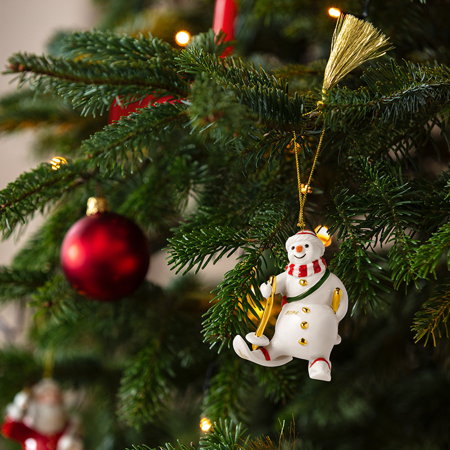 Villeroy & Boch snømann-ornament 2026 henger på et pyntet juletre med røde julekuler