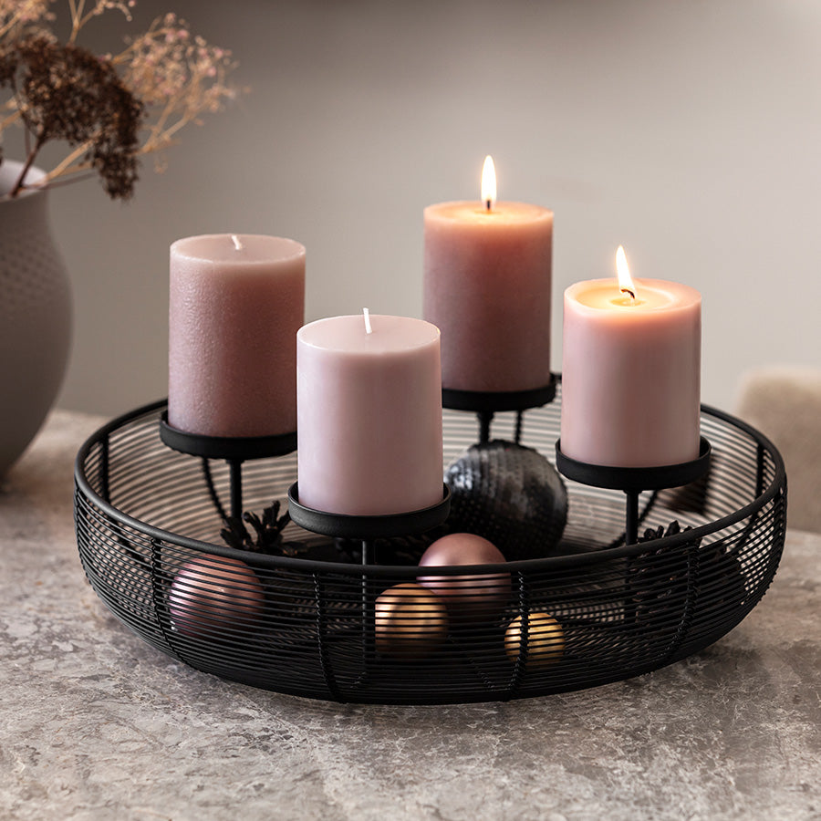 Rund svart adventsstake med fire rosa kubbelys og juledekorasjoner på bordet