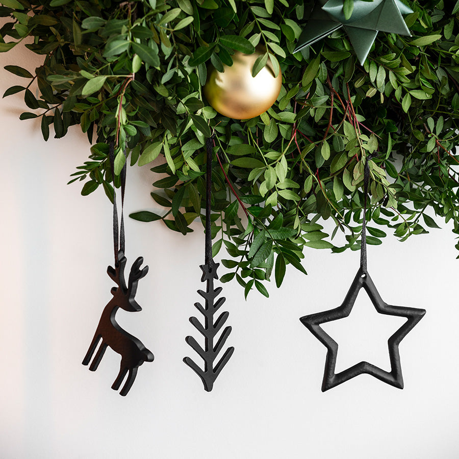 Svarte Christmas Chic juleornamenter fra Villeroy & Boch henger på en grønn julekrans sammen med en gullfarget julekule