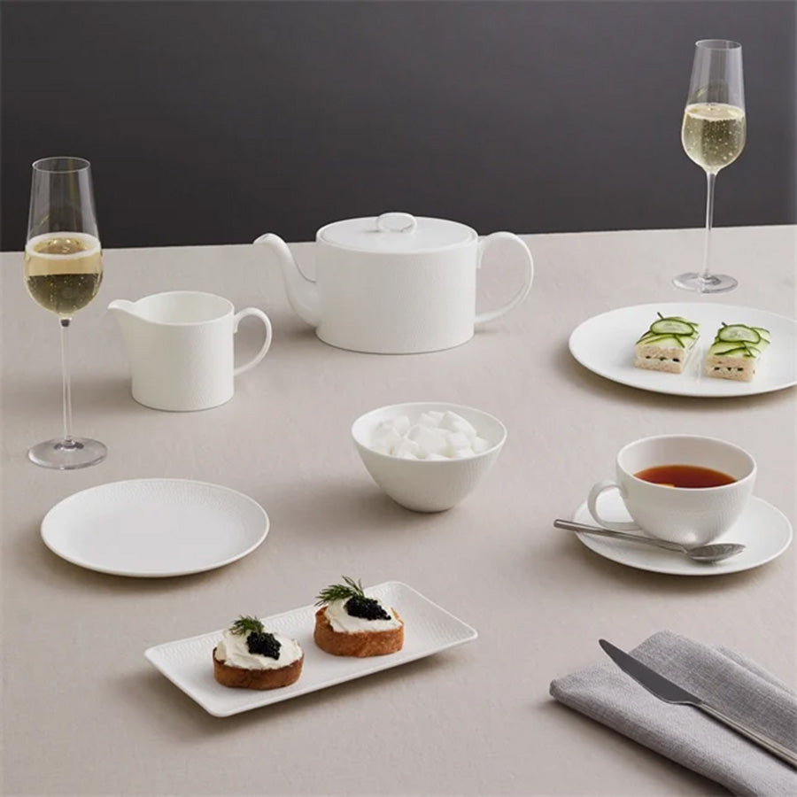 Elegant borddekorasjon med Wedgwood Gio tekanne i benporselen, sammen med stilige glass, en melkekanne og delikate tallerkener med mat, perfekt for en sofistikert te-stund.
