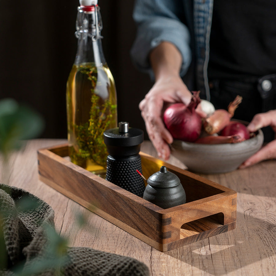 Bruk av serveringsbrett i akasietre med olivenolje, krydderkverner og en bolle med grønnsaker, perfekt til borddekking.