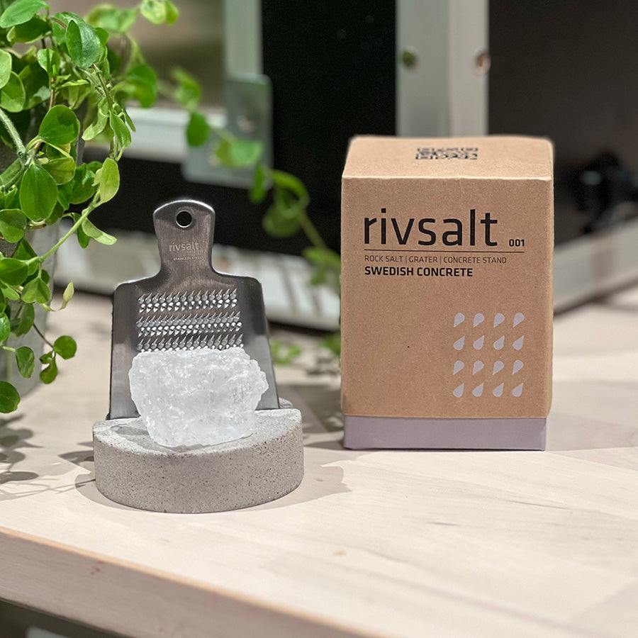 Adelante Rivsalt sett med halittsaltstein, rivjern i rustfritt stål, og emballasje i bakgrunnen, alt med fokus på svensk betongdesign.