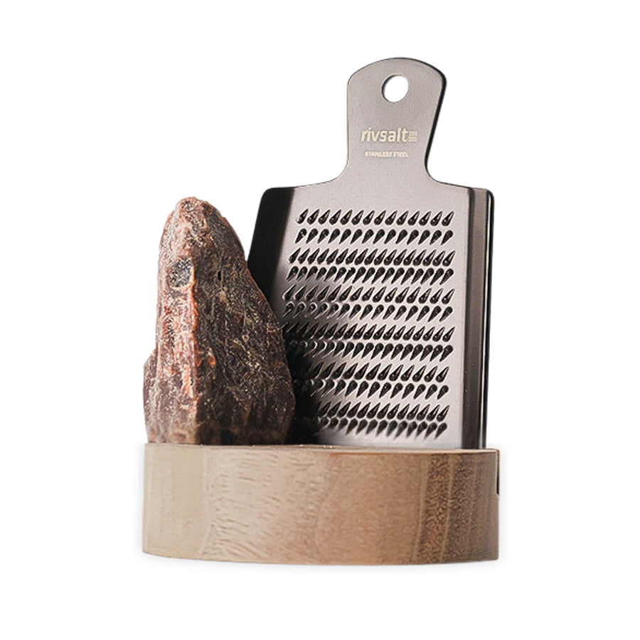 Adelante Rivsalt Kala Namak m/stativ Valnøtt + Rivjern, med en rustfritt stål rivjern og en stor saltstein i et elegant valnøttstativ, ideelt for aromatisk salting av mat.