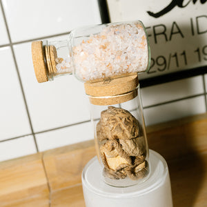 Adelante Rivsalt Rock Salt Blend i en glassbeholder med kork, plassert oppå en annen beholder med sopp. Stilig og funksjonell oppbevaring av salt.