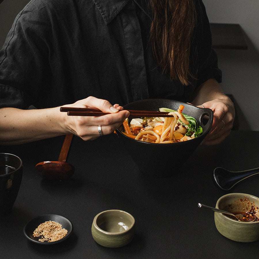 Kvinne som nyter ramen i en stilig ramenbolle fra Antei, med spisepinner i hånden.