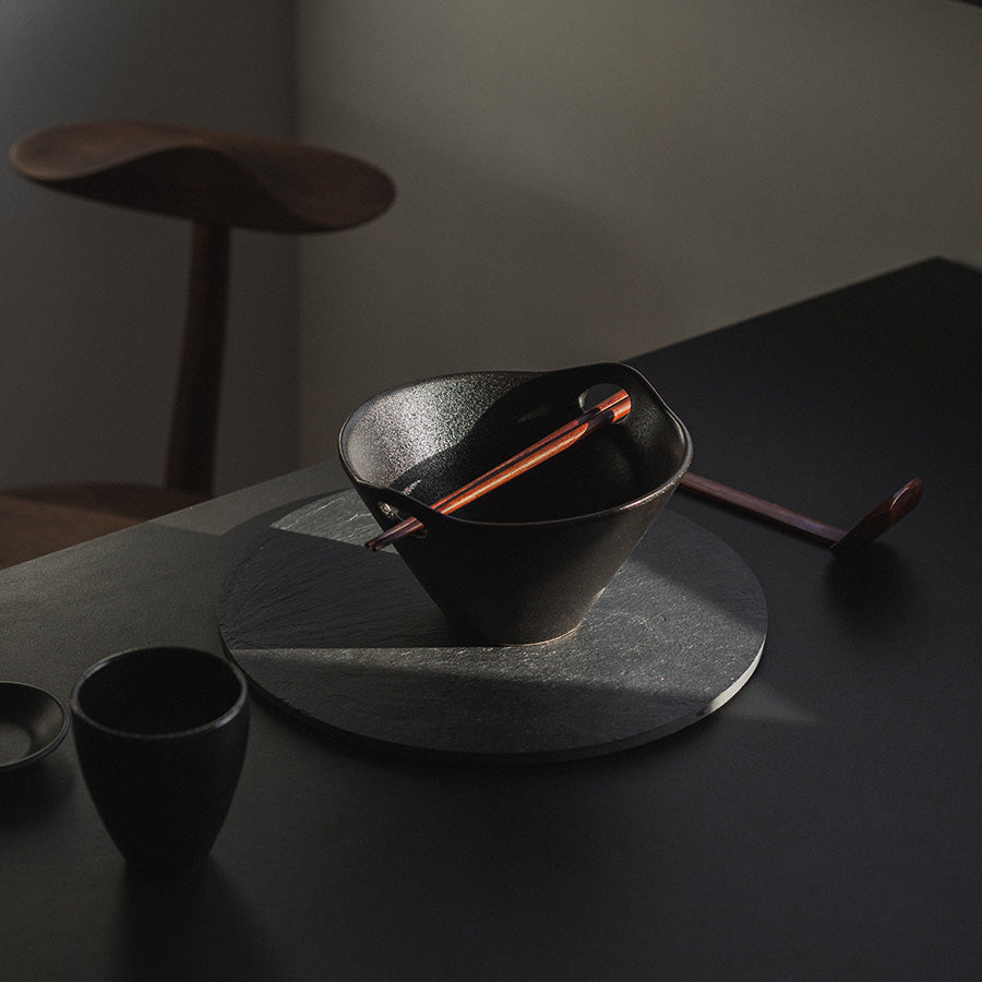 Ramenbolle med skje og spisepinner plasert på en svart overflate, skaper en elegant serveringsopplevelse.