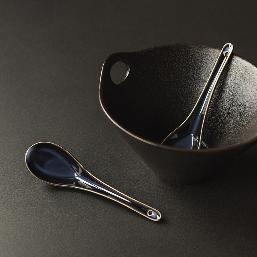 Antei Menka ris- og suppeskje plassert i en svart bolle, fremhever det klassiske asiatiske designet.