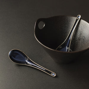 Antei Menka ris- og suppeskje plassert i en svart bolle, fremhever det klassiske asiatiske designet.