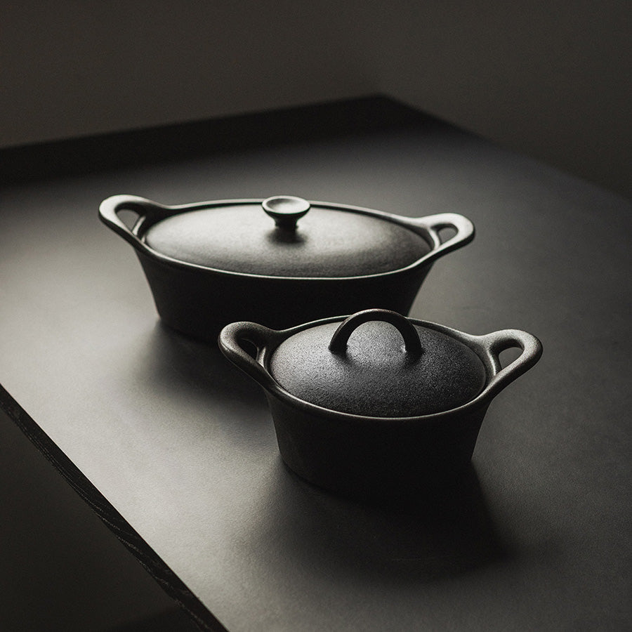 To stilfulle ildfaste former i sort, en stor oval og en liten rund med lokk, ideelle for matlaging.