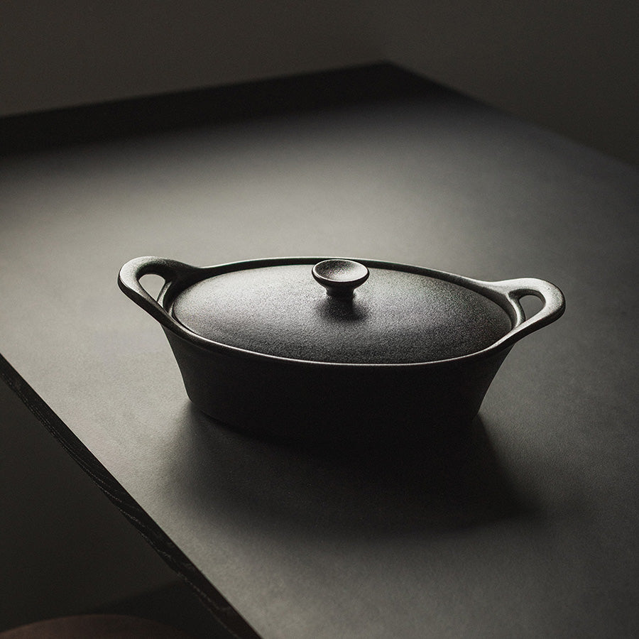 Elegant oval ildfast form med lokk i sort, plassert på et bord for enkel servering.