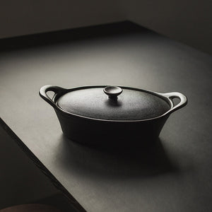 Elegant oval ildfast form med lokk i sort, plassert på et bord for enkel servering.