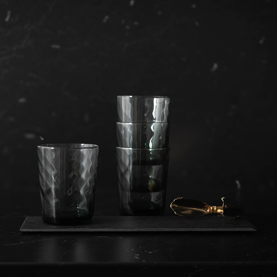 Stabelbare sotete vannglass fra Ask Jade, elegant plassert på en svart bakgrunn med tilbehør.