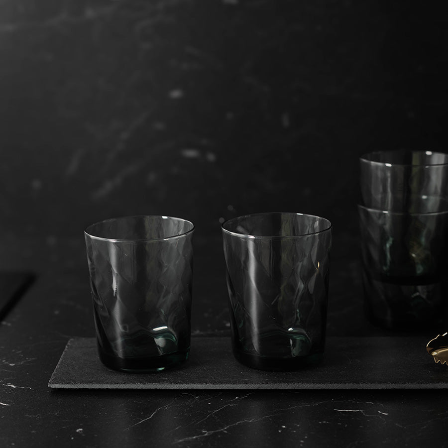 To sotete vannglass i fokus, med stabelbare vannglass i bakgrunnen, perfekt for enhver borddekorasjon.