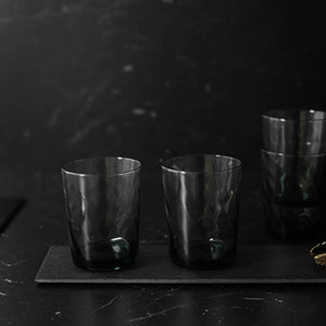 To sotete vannglass i fokus, med stabelbare vannglass i bakgrunnen, perfekt for enhver borddekorasjon.