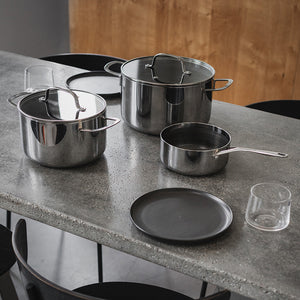 As Kull grytesett utstilt på en moderne bordflate, med tre rustfrie gryter, inkludert lokk. Ideelt for praktisk og inspirerende matlaging med lite fett.