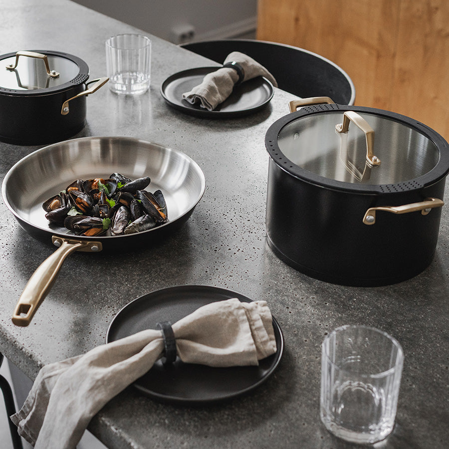 Grytesett fra Ask Obsidian på kjøkkenbord, med gryte, stekepanne og dekket bord for en middag.